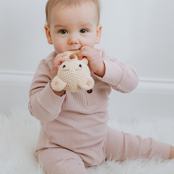 A baby wearing a pink long sleeve ribbed cotton romper, sitting and holding a toy.