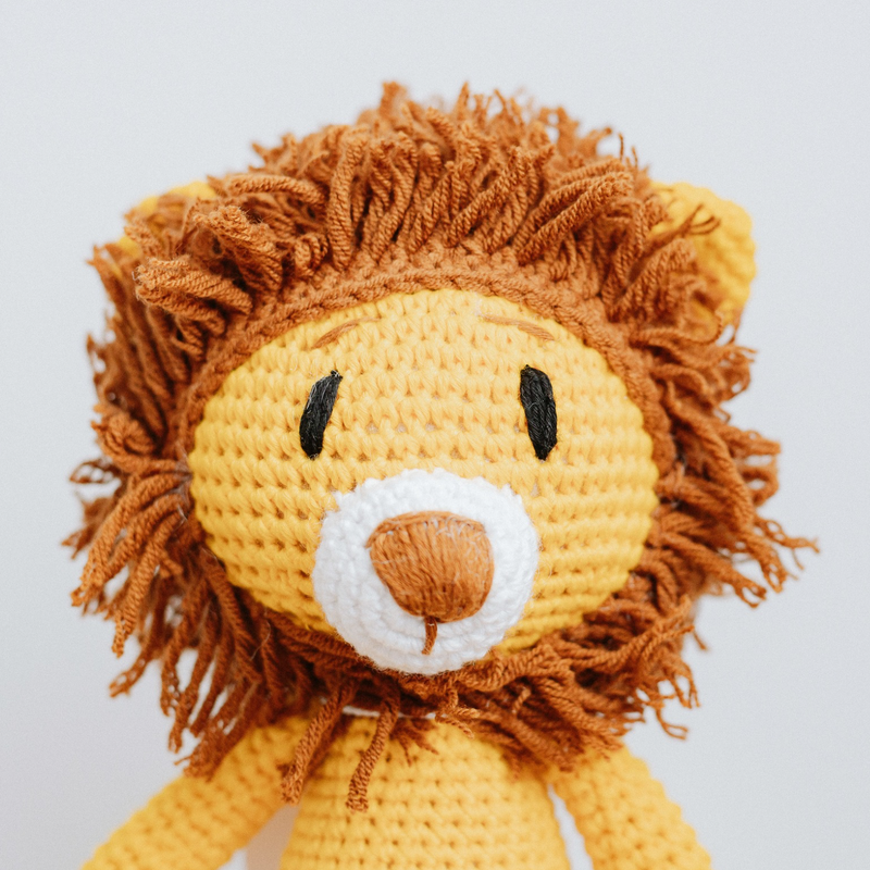 A handmade crochet toy resembling a lion with a yellow body and brown mane.